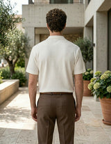 Man wearing a white shirt and brown pants standing in a garden setting.