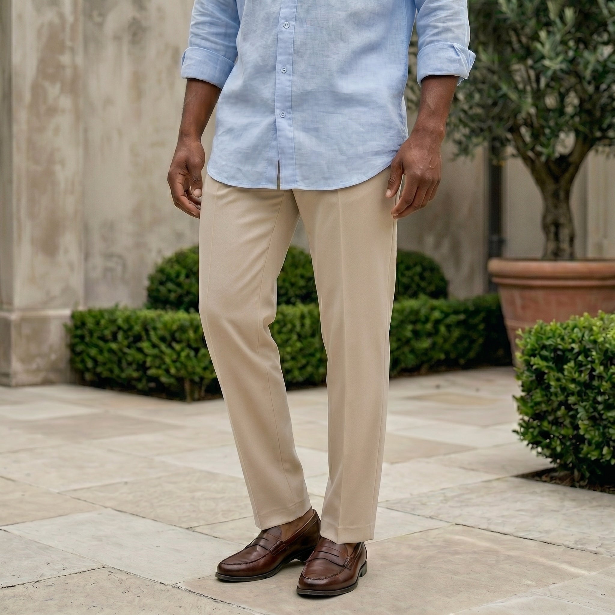 Men wearing a light blue shirt, beige pants, and brown shoes standing outdoors.