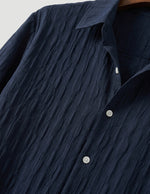 Navy blue textured shirt with white buttons on a neutral background