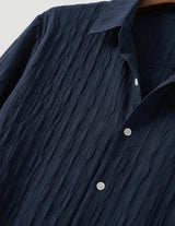 Navy blue textured shirt with white buttons on a neutral background