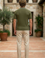 Olivo - Man wearing a green polo shirt and beige pants standing in a stone-walled courtyard with potted plants.