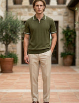 Olivo - Man wearing a green polo shirt and beige pants standing in an outdoor setting with stone walls and potted plants.