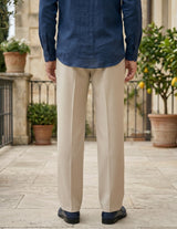 Person wearing a blue shirt and beige pants standing outdoors with plants in the background