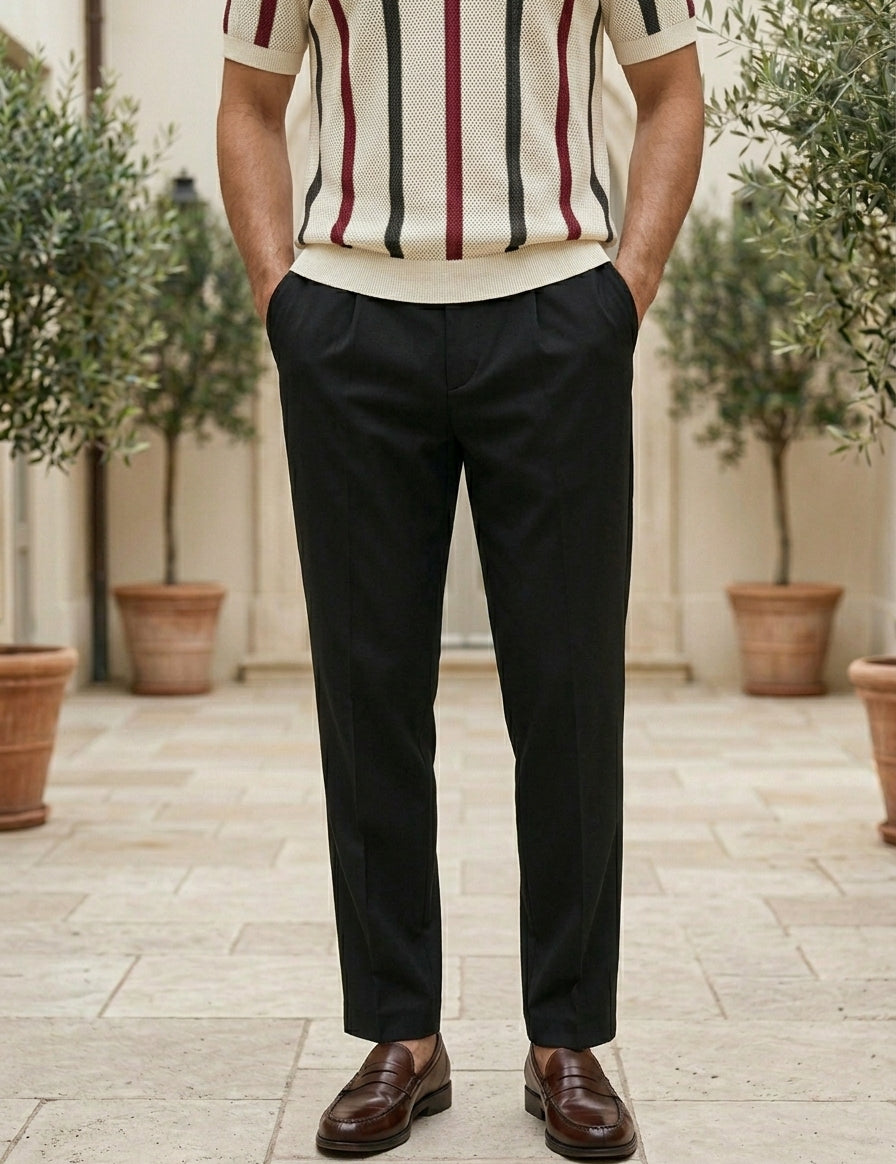 Person wearing a striped shirt and black pants standing outdoors with plants in the background