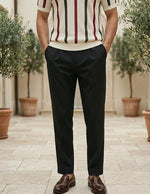 Person wearing a striped shirt and black pants standing outdoors with plants in the background