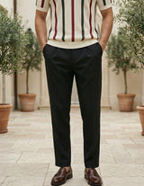 Person wearing a striped shirt and black pants standing outdoors with plants in the background