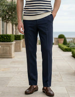 Person wearing a striped shirt and navy pants standing on a patio with greenery and ocean view.