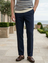 Person wearing a striped shirt and navy pants standing on a patio with greenery and ocean view.