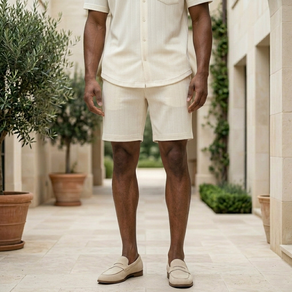 Person wearing a white outfit standing in an outdoor setting with plants and stone pavement.