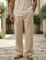 Person wearing beige linen pants and shirt standing on a stone path with greenery in the background