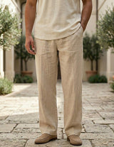 Person wearing beige linen pants and shirt standing on a stone path with greenery in the background