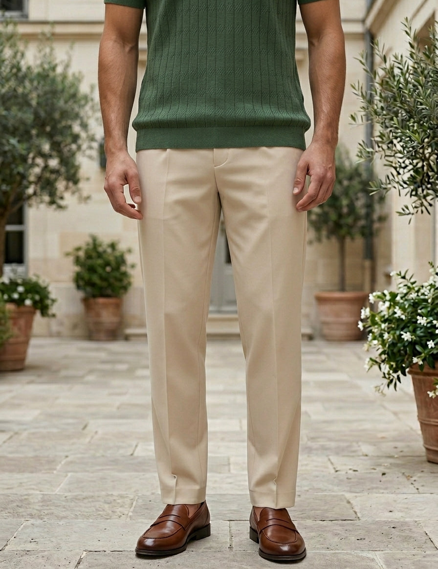 Person wearing beige pants and a green shirt standing outdoors with plants in the background