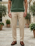 Person wearing beige pants and a green shirt standing outdoors with plants in the background