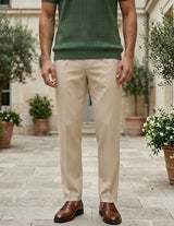 Person wearing beige pants and a green shirt standing outdoors with plants in the background