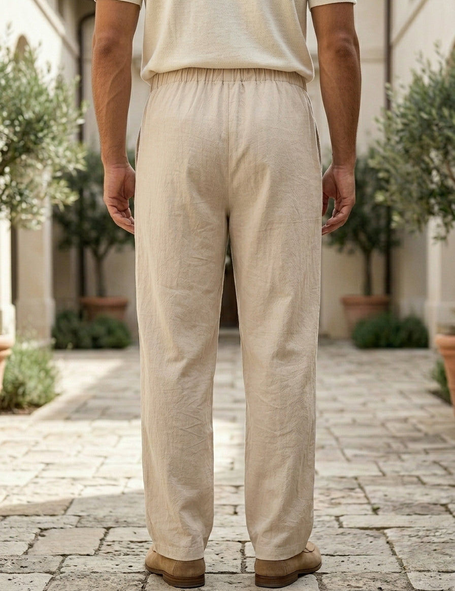 Person wearing beige pants and a light-colored shirt standing on a stone pavement with plants in the background.