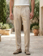 Person wearing beige pants standing on a stone path with plants and buildings in the background