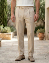 Person wearing beige pants standing on a stone path with plants and buildings in the background