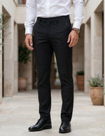 Person wearing black pants and a white shirt in an outdoor setting with plants.