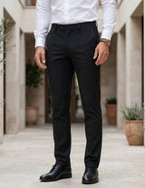 Person wearing black pants and a white shirt in an outdoor setting with plants.