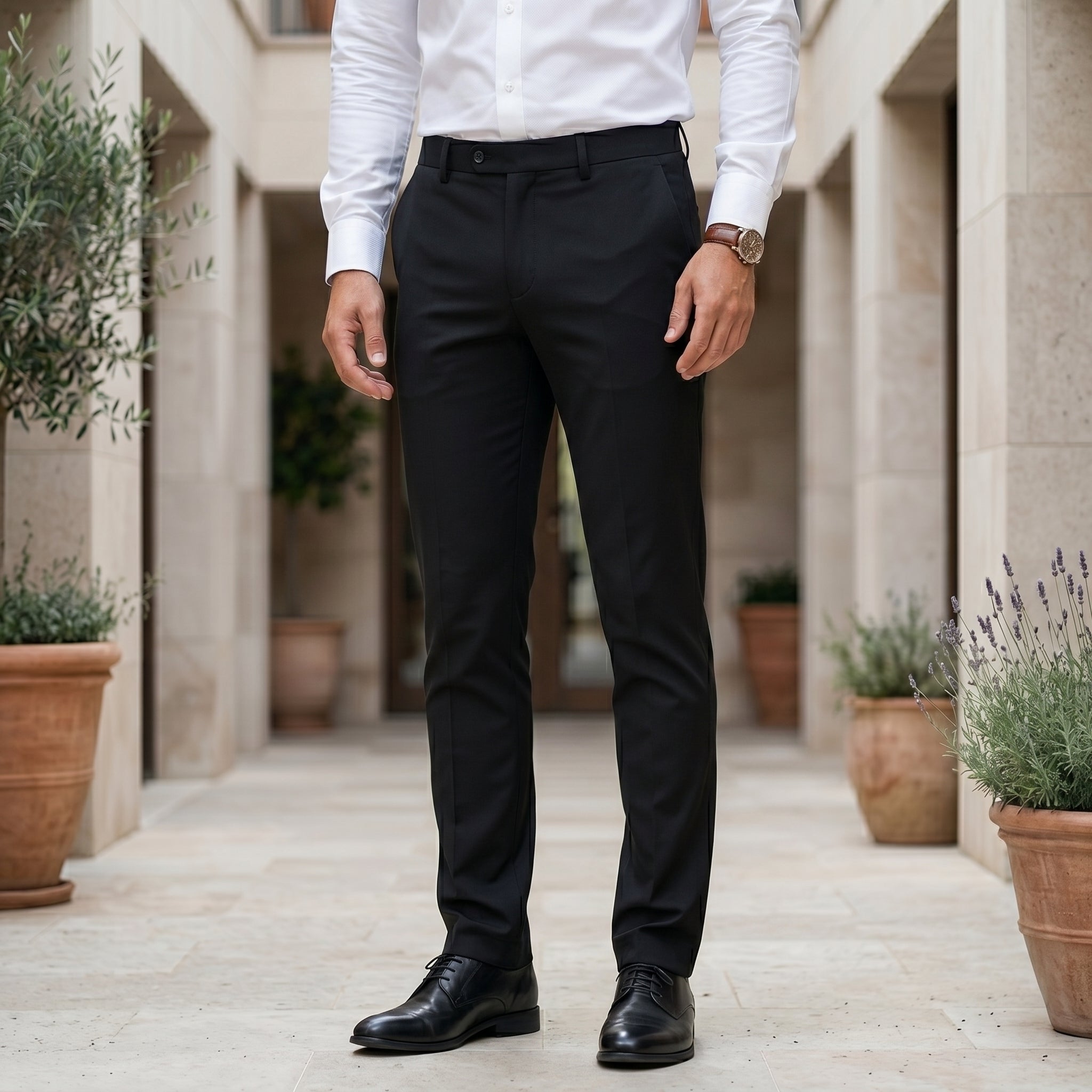 Person wearing black pants and a white shirt in an outdoor setting with plants.