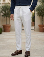 Person wearing white linen pants with a navy shirt and brown shoes outdoors.