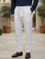 Person wearing white linen pants with a navy shirt and brown shoes outdoors.