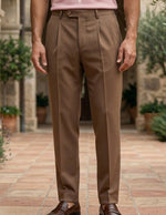 Rosato - Person wearing brown trousers standing in a courtyard with stone architecture and greenery.