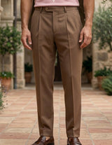 Rosato - Person wearing brown trousers standing in a courtyard with stone architecture and greenery.