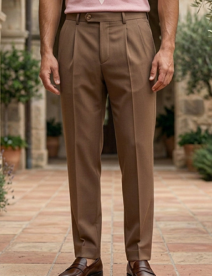 Rosato - Person wearing brown trousers standing in a courtyard with stone architecture and greenery.