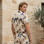 Side view of male model wearing an ivory abstract print short-sleeve shirt with matching shorts.
