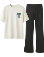 White t-shirt with graphic design and black pants on a light gray background