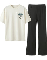 White t-shirt with graphic design and black pants on a light gray background