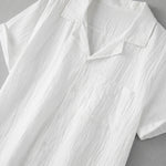 White textured short-sleeve button-up summer shirt with camp collar and chest pocket laid flat.