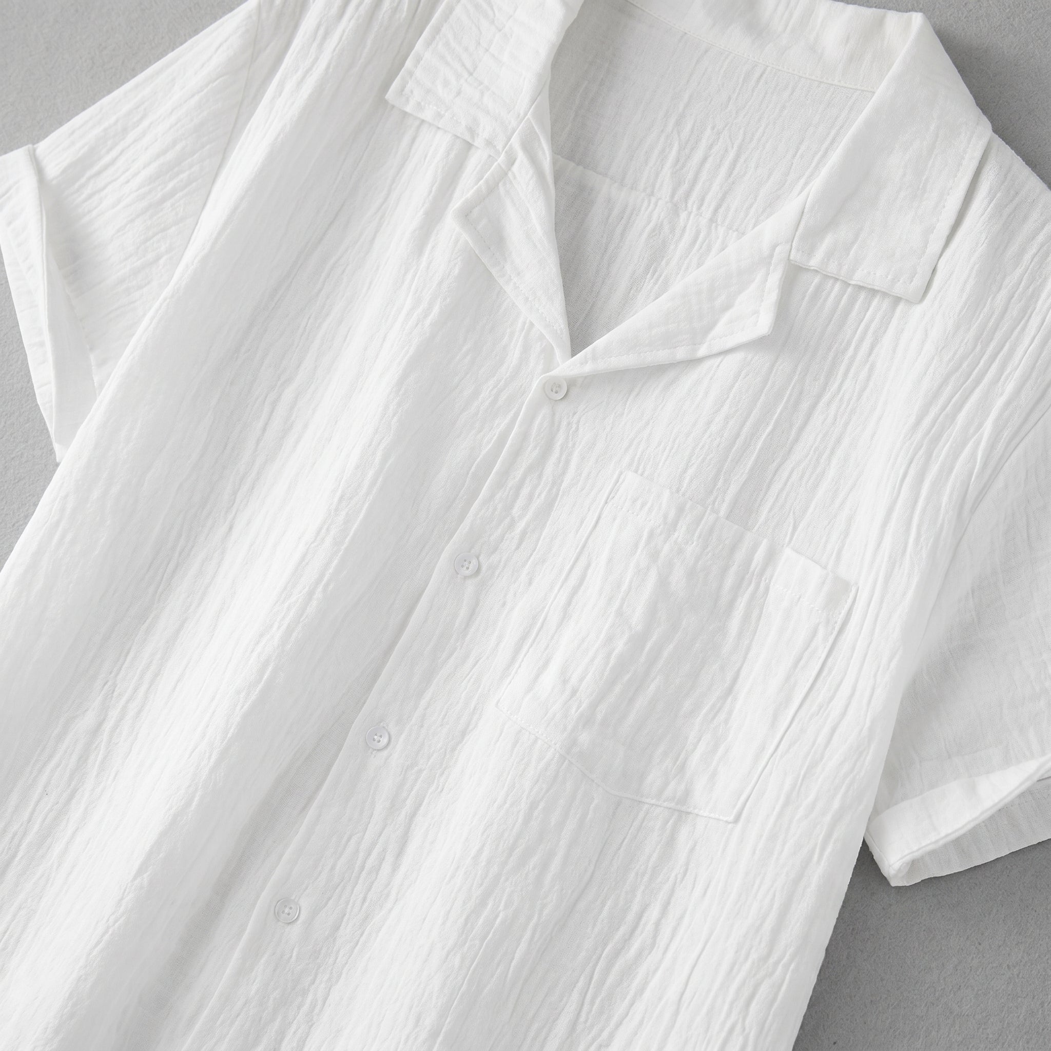 White textured short-sleeve button-up summer shirt with camp collar and chest pocket laid flat.
