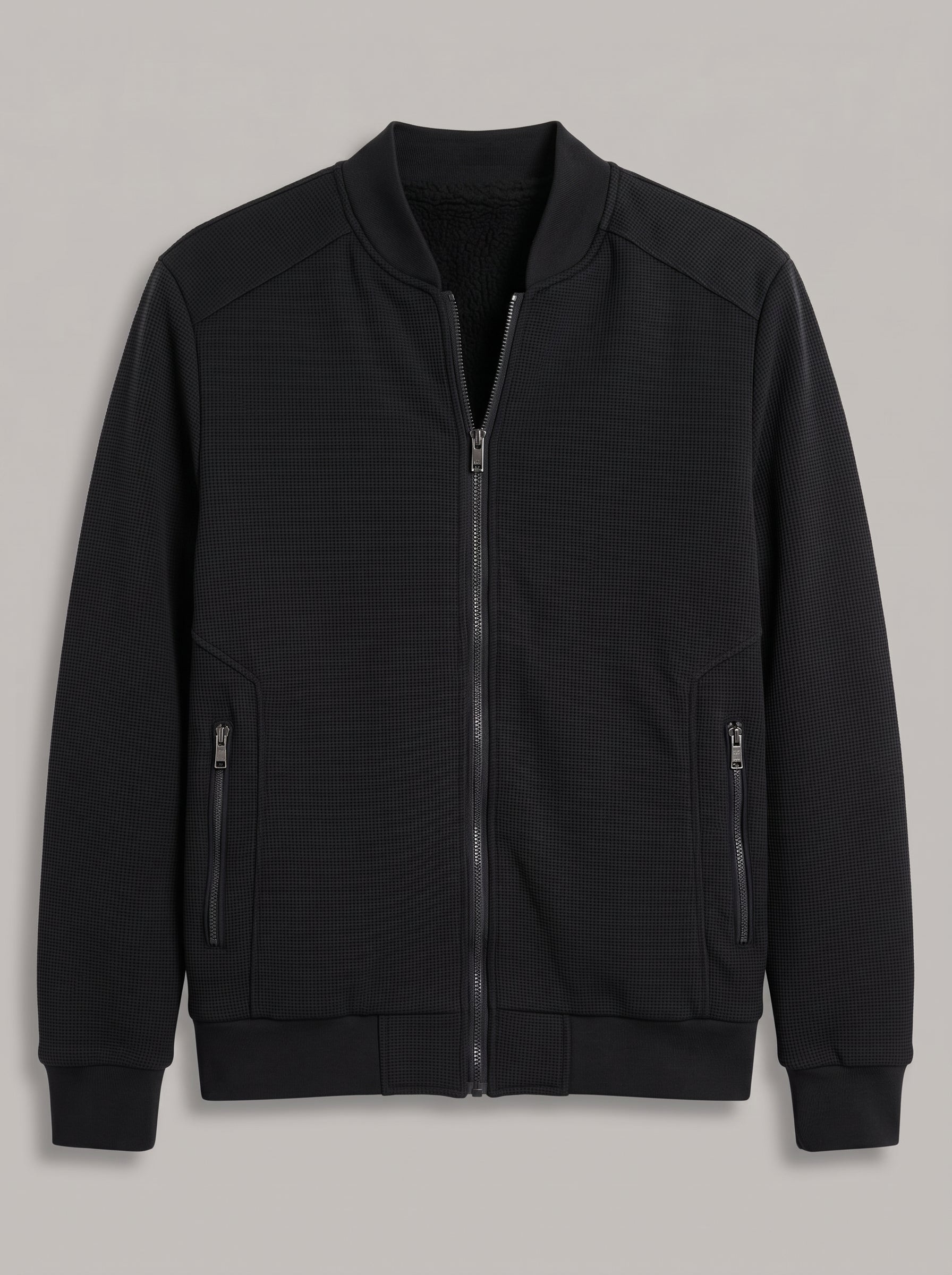 A black zip-up bomber jacket with a ribbed collar, cuffs, and hem, featuring two vertical zippered pockets on the sleeves, shown against a neutral gray background.